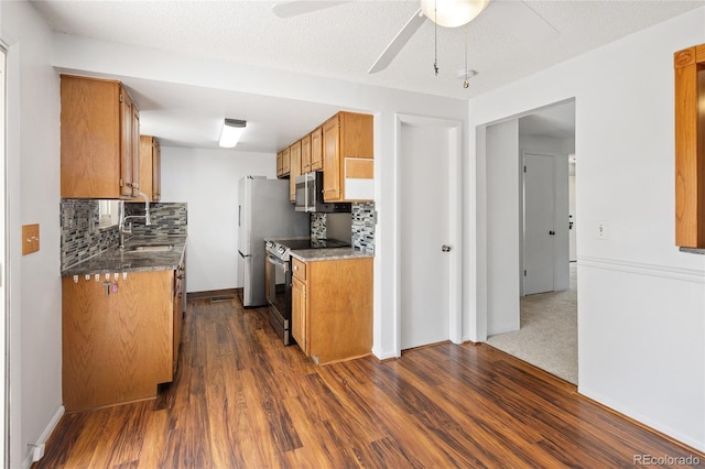 kitchen featuring a ceiling fan, dark wood-style flooring, a sink, stainless steel appliances, and tasteful backsplash