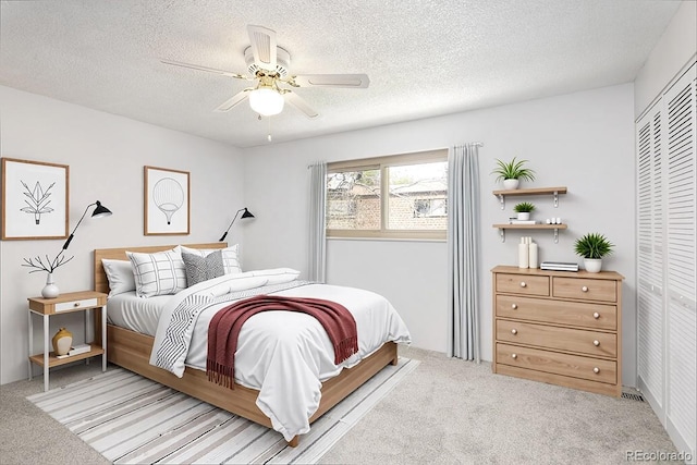 bedroom featuring light colored carpet, a textured ceiling, a closet, and ceiling fan
