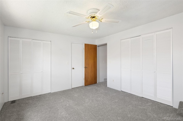 unfurnished bedroom featuring two closets, a textured ceiling, carpet flooring, and a ceiling fan