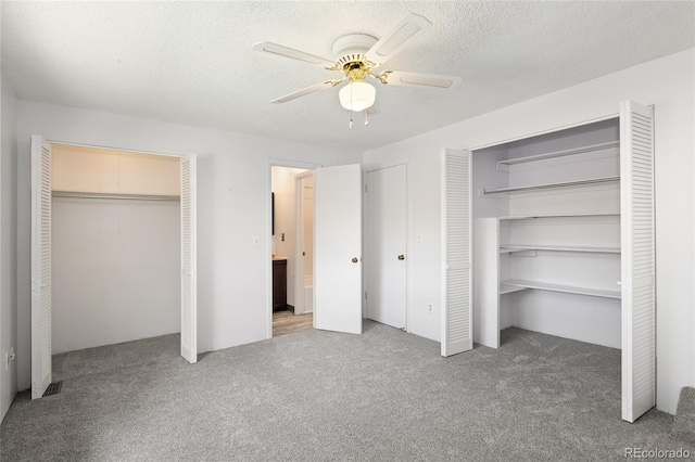 unfurnished bedroom featuring carpet flooring, two closets, a ceiling fan, and a textured ceiling