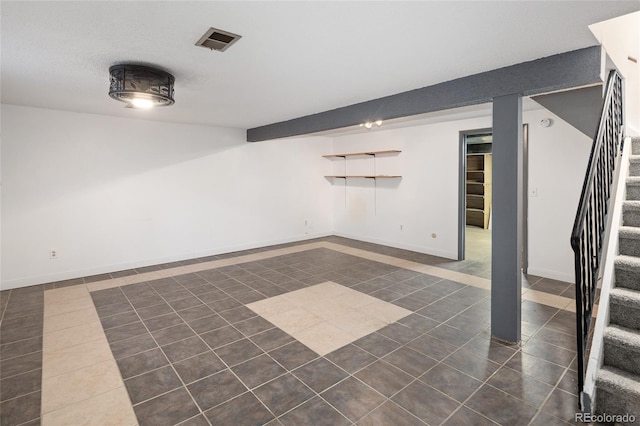 finished below grade area featuring stairs, dark tile patterned floors, baseboards, and visible vents