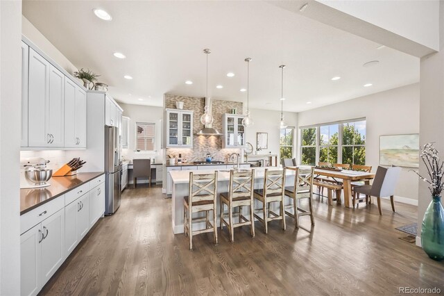 10401 Maplebrook Way, Highlands Ranch, CO 80126 - kitchen featuring stainless steel appliances, decorative backsplash, wall chimney exhaust hood, a kitchen bar, and dark wood-type flooring