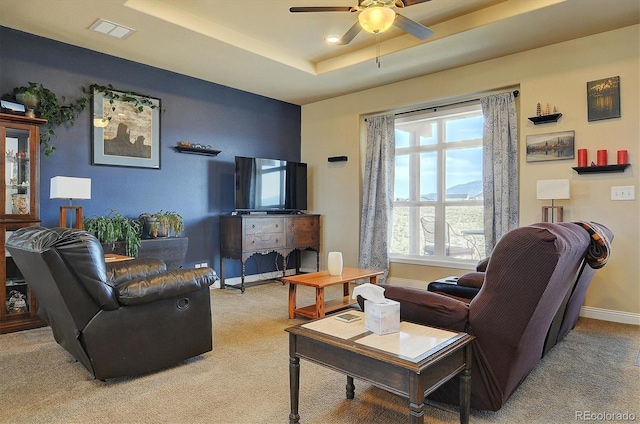 living room featuring visible vents, baseboards, a ceiling fan, a tray ceiling, and light colored carpet