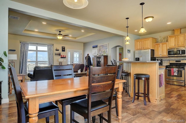 dining area with arched walkways, visible vents, wood finished floors, and a raised ceiling