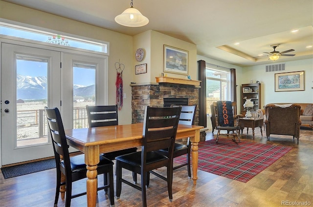 dining space featuring a tray ceiling, a ceiling fan, a stone fireplace, visible vents, and wood finished floors