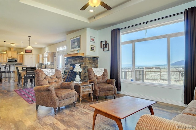 living area featuring baseboards, recessed lighting, light wood-style flooring, a ceiling fan, and a raised ceiling