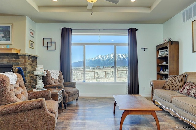 living area with ceiling fan, visible vents, wood finished floors, a raised ceiling, and a mountain view