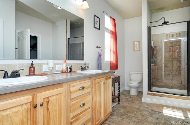 bathroom with a shower stall, double vanity, a sink, and toilet