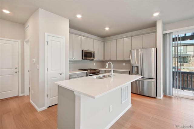 kitchen with sink, an island with sink, stainless steel appliances, and light wood-type flooring