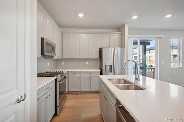 kitchen featuring tasteful backsplash, light stone counters, appliances with stainless steel finishes, light hardwood / wood-style floors, and sink