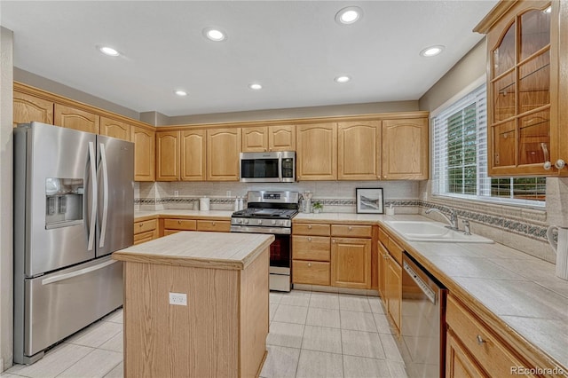 kitchen with appliances with stainless steel finishes, tile countertops, sink, a center island, and light tile patterned floors