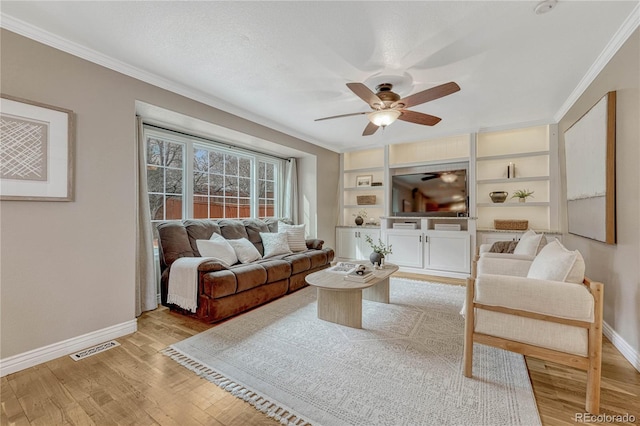 living room with built in shelves, ceiling fan, ornamental molding, and light wood-type flooring