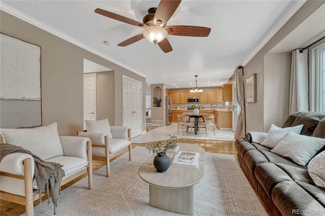 living room featuring crown molding, ceiling fan with notable chandelier, and light hardwood / wood-style floors