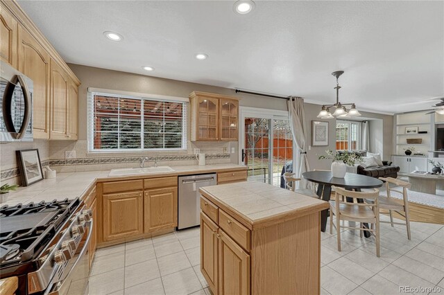 kitchen with a kitchen island, appliances with stainless steel finishes, pendant lighting, sink, and tile counters