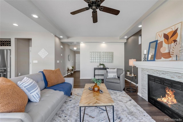 living room with ceiling fan, dark hardwood / wood-style flooring, and a stone fireplace