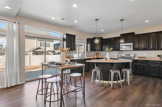 kitchen with hanging light fixtures, dark hardwood / wood-style floors, a kitchen bar, a kitchen island, and appliances with stainless steel finishes