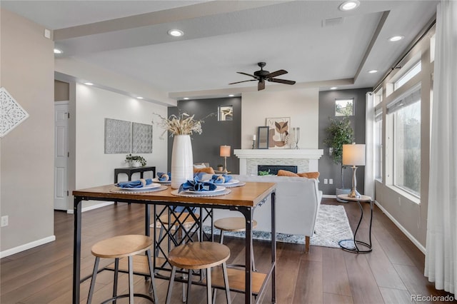 dining room featuring a fireplace, a raised ceiling, ceiling fan, and dark wood-type flooring