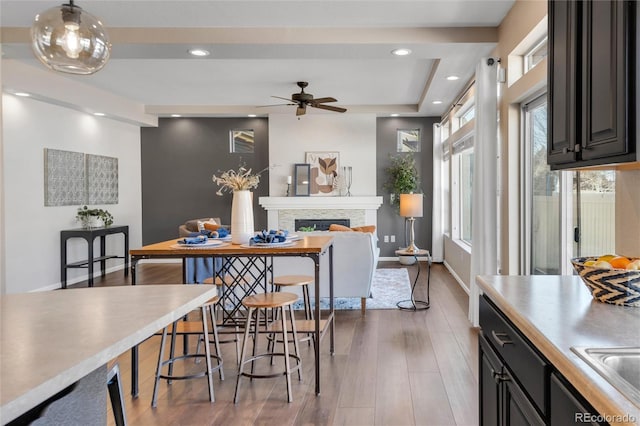 dining area featuring a raised ceiling, a stone fireplace, sink, hardwood / wood-style flooring, and ceiling fan