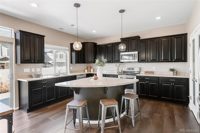 kitchen with a center island, dark hardwood / wood-style floors, decorative light fixtures, a breakfast bar, and appliances with stainless steel finishes