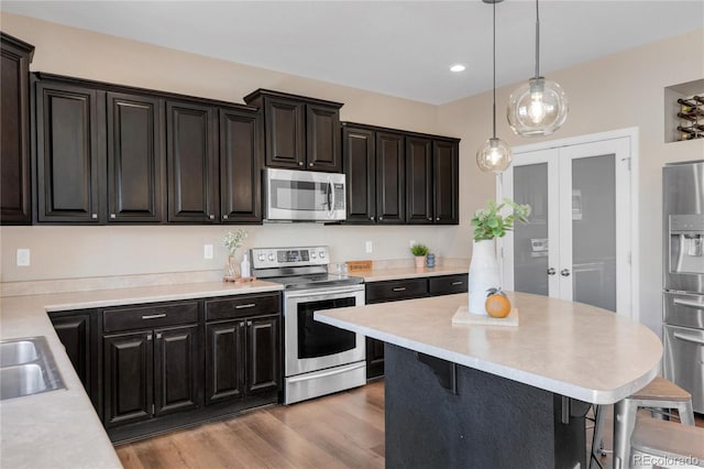 kitchen featuring a kitchen bar, appliances with stainless steel finishes, french doors, light hardwood / wood-style flooring, and hanging light fixtures