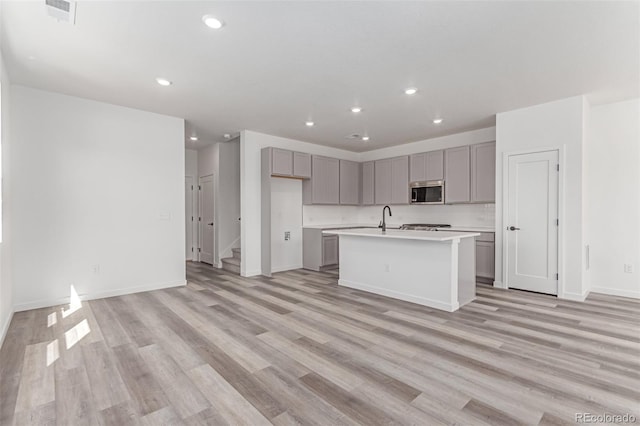 kitchen featuring stainless steel microwave, gray cabinets, recessed lighting, light countertops, and a kitchen island with sink