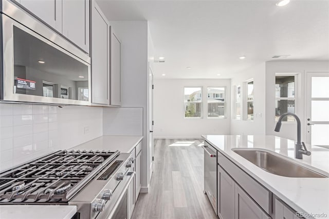 kitchen featuring appliances with stainless steel finishes, a sink, light wood-type flooring, tasteful backsplash, and gray cabinetry