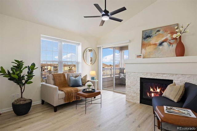 sitting room with lofted ceiling, a stone fireplace, light hardwood / wood-style floors, and ceiling fan