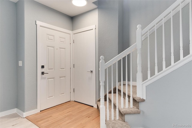 foyer entrance with stairs, wood finished floors, and baseboards