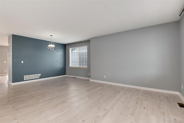 spare room with a chandelier, light wood-type flooring, visible vents, and baseboards