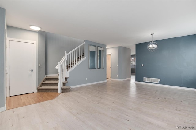 spare room featuring a notable chandelier, visible vents, stairway, wood finished floors, and baseboards