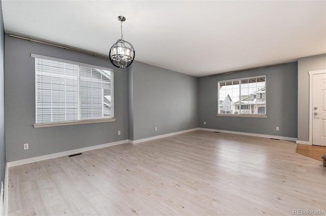 empty room with light wood-style floors, visible vents, a notable chandelier, and baseboards