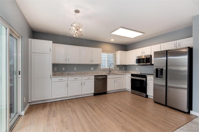 kitchen with white cabinets, stainless steel appliances, light wood-type flooring, pendant lighting, and a sink