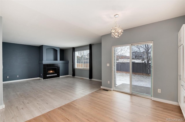 unfurnished living room with light wood-style floors, a chandelier, baseboards, and a tiled fireplace