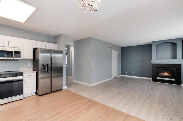 kitchen featuring appliances with stainless steel finishes, visible vents, a tiled fireplace, and white cabinetry