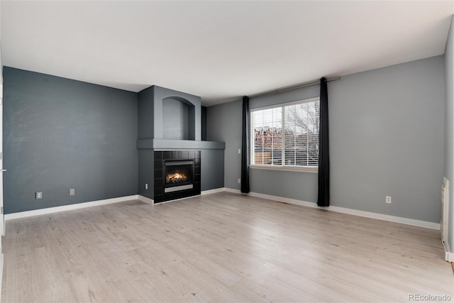 unfurnished living room with a tile fireplace, baseboards, and wood finished floors