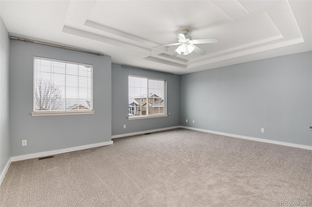 empty room with baseboards, a tray ceiling, and carpet flooring