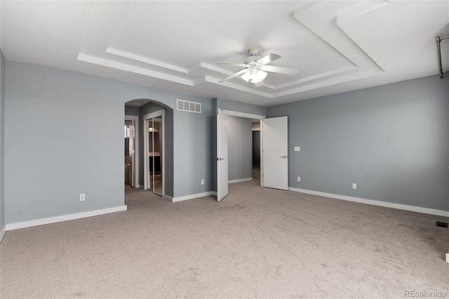 unfurnished bedroom with a tray ceiling, visible vents, arched walkways, and baseboards