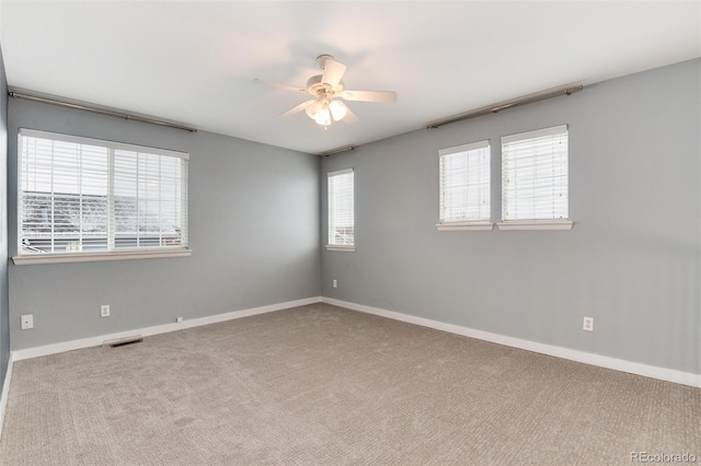 unfurnished room with carpet, baseboards, visible vents, and a wealth of natural light