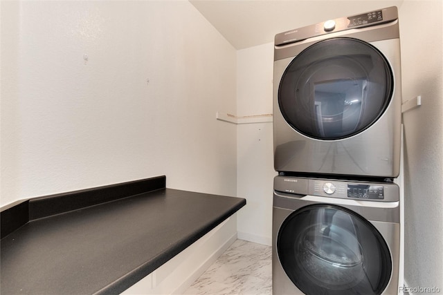 clothes washing area featuring marble finish floor, stacked washer and dryer, laundry area, and baseboards