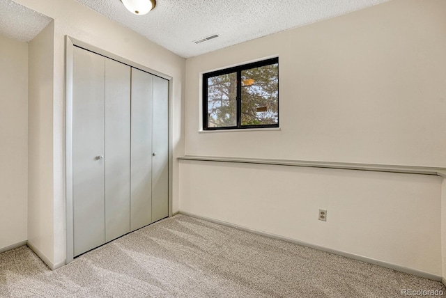 unfurnished bedroom featuring light colored carpet, a closet, and a textured ceiling