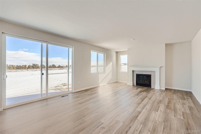 unfurnished living room featuring light wood-style floors, a tile fireplace, a healthy amount of sunlight, and visible vents