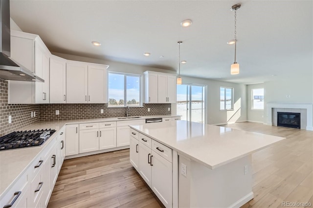 kitchen featuring wall chimney exhaust hood, stainless steel gas stovetop, light wood-style flooring, and a sink