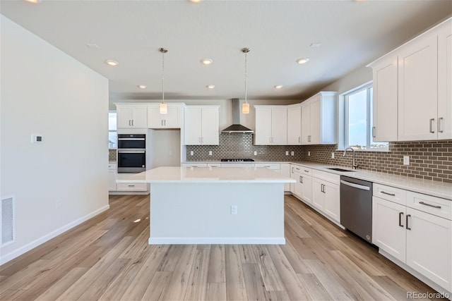 kitchen with light wood finished floors, white cabinets, stainless steel appliances, wall chimney range hood, and a sink