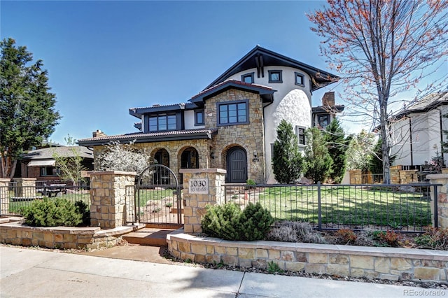 view of front of property featuring a tile roof, a fenced front yard, a gate, stone siding, and stucco siding