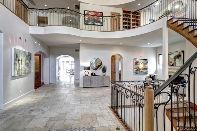 foyer entrance featuring stone tile flooring, arched walkways, baseboards, recessed lighting, and a high ceiling