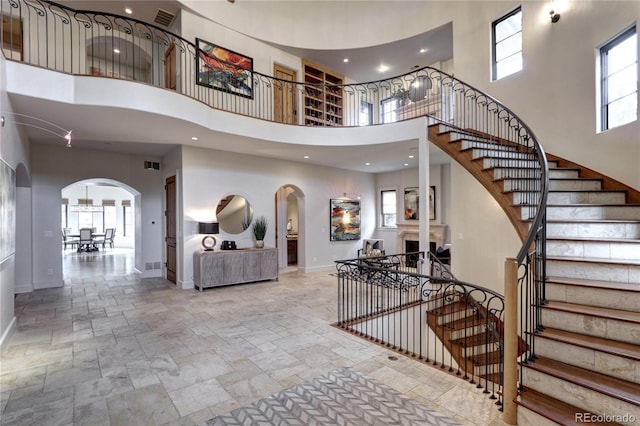 foyer featuring arched walkways, stone tile flooring, a towering ceiling, and baseboards