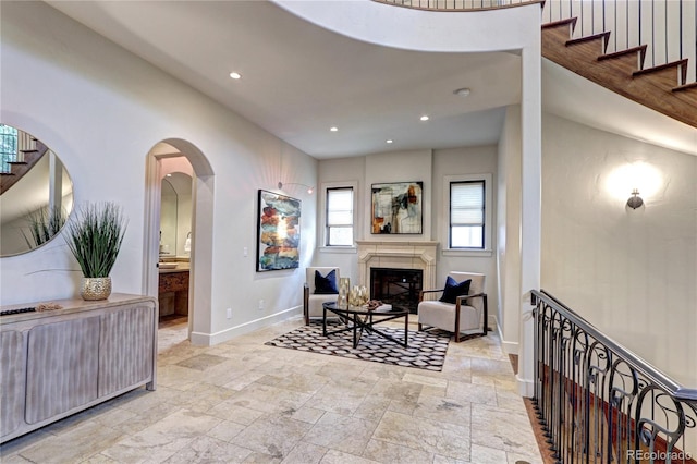 interior space featuring stone tile floors, a glass covered fireplace, arched walkways, baseboards, and recessed lighting