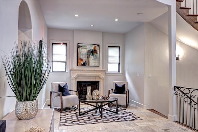 living area featuring baseboards, stone tile floors, a glass covered fireplace, and plenty of natural light