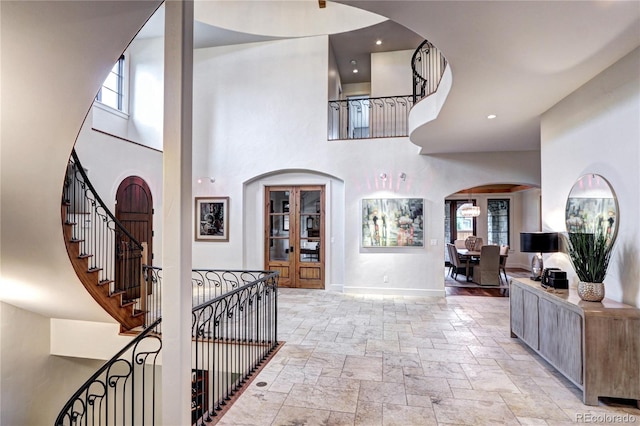 entryway with stairway, stone tile floors, arched walkways, a towering ceiling, and baseboards