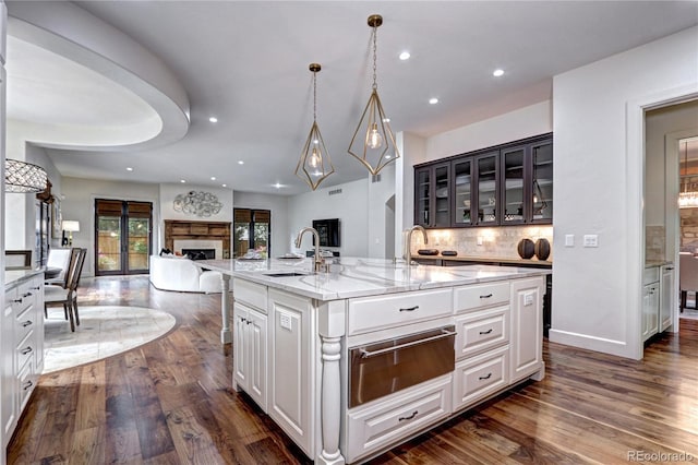 kitchen with a sink, dark wood-type flooring, a warming drawer, a kitchen island with sink, and open floor plan